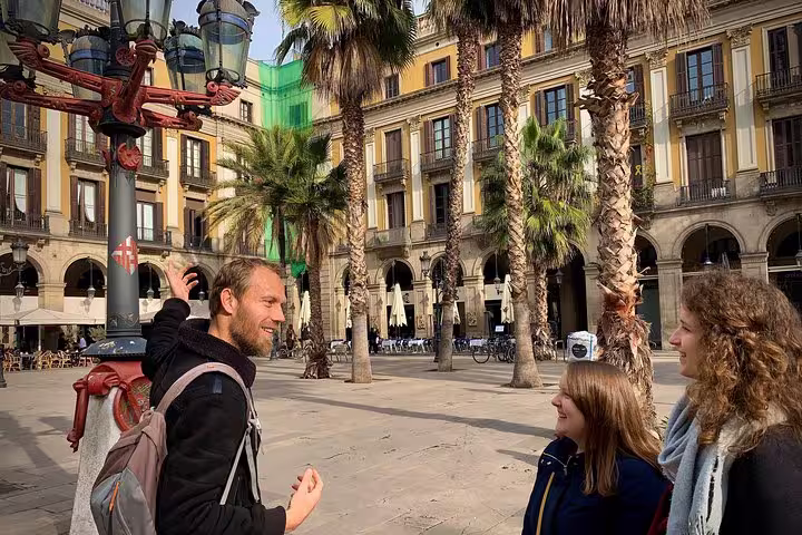 Tour guide leading a group in Barcelona's historic Plaça Reial, showcasing vibrant architecture and palm trees.