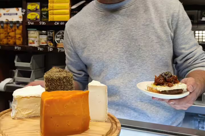 Selection of artisanal cheeses with a person holding a tapas plate in a local Barcelona shop during a wine tour.