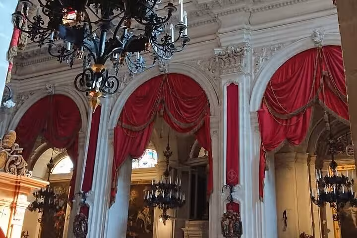 Ornate interior of a Baroque church with red draped arches and chandeliers, highlighting artistic elegance in Noto.