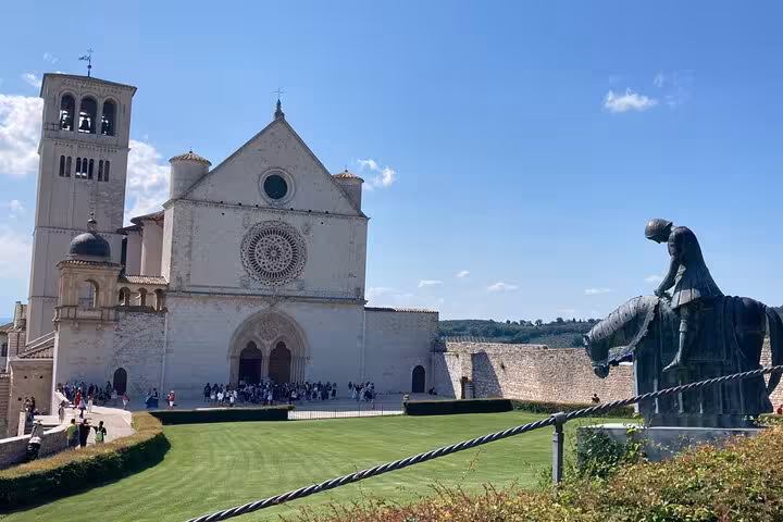 The Basilica of Saint Francis of Assisi with a striking statue in the foreground on a sunny day tour from Rome.