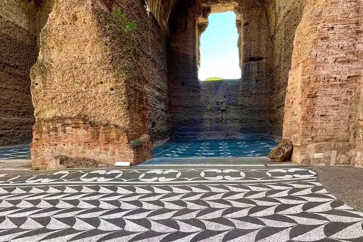 Intricate black and white geometric floor mosaics framed by towering ruins at the Baths of Caracalla in Rome