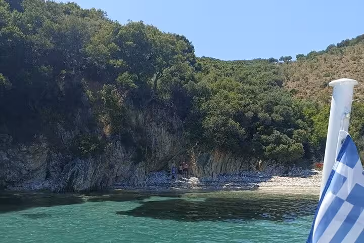 Hidden Ionian Sea cove with turquoise water seen from BBQ boat tour by locals, Greek flag at the bow