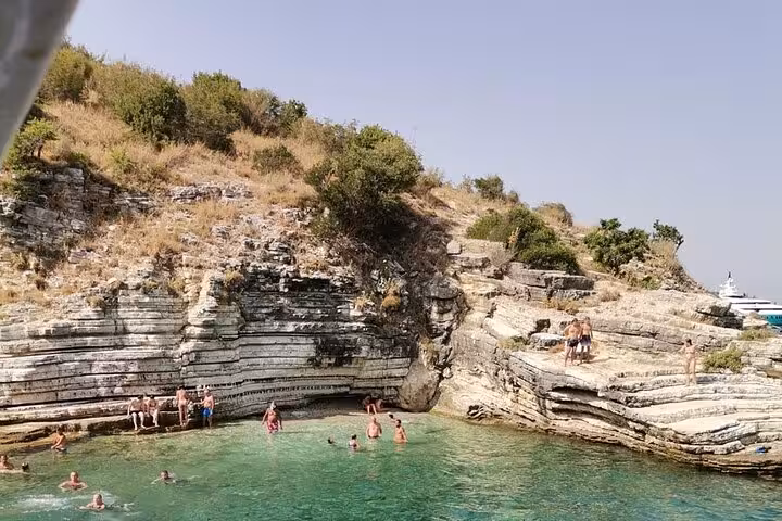 Swimmers in a rocky Ionian Sea cove during a locals BBQ boat tour, crystal-clear water and cliff ledges