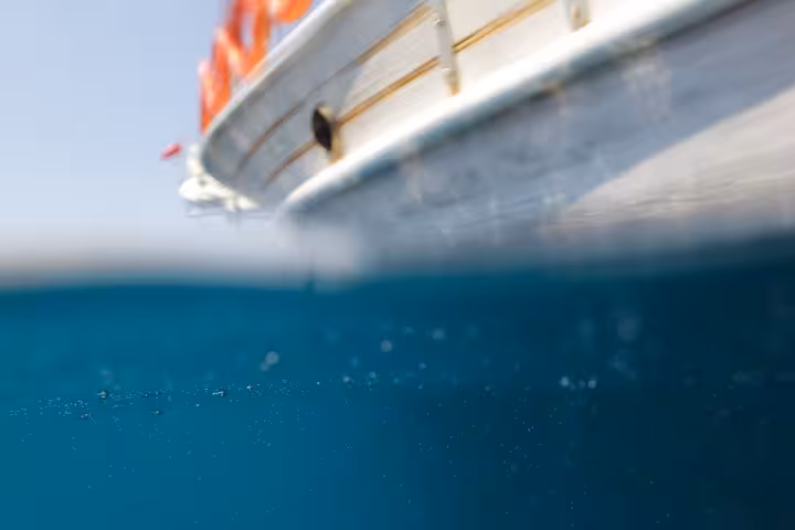 Half-underwater view beside a boat in crystal-clear Ionian Sea, swimming stop on locals BBQ boat tour