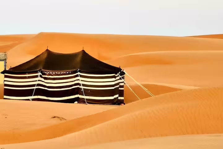 Traditional Bedouin tent nestled among the golden dunes of Wahiba Sands on a private desert camping tour from Muscat.