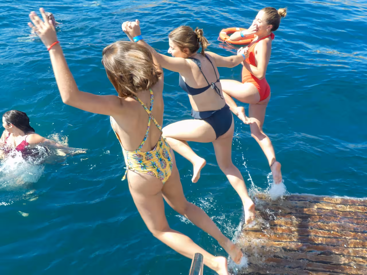 Excited guests jumping into crystal-clear turquoise Atlantic Ocean during Portimao Benagil catamaran swimming stop