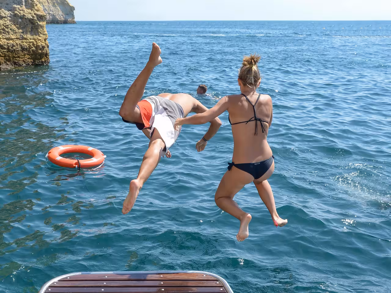 Excited guests jumping into turquoise Atlantic waters during a Portimao catamaran coastline tour near Benagil