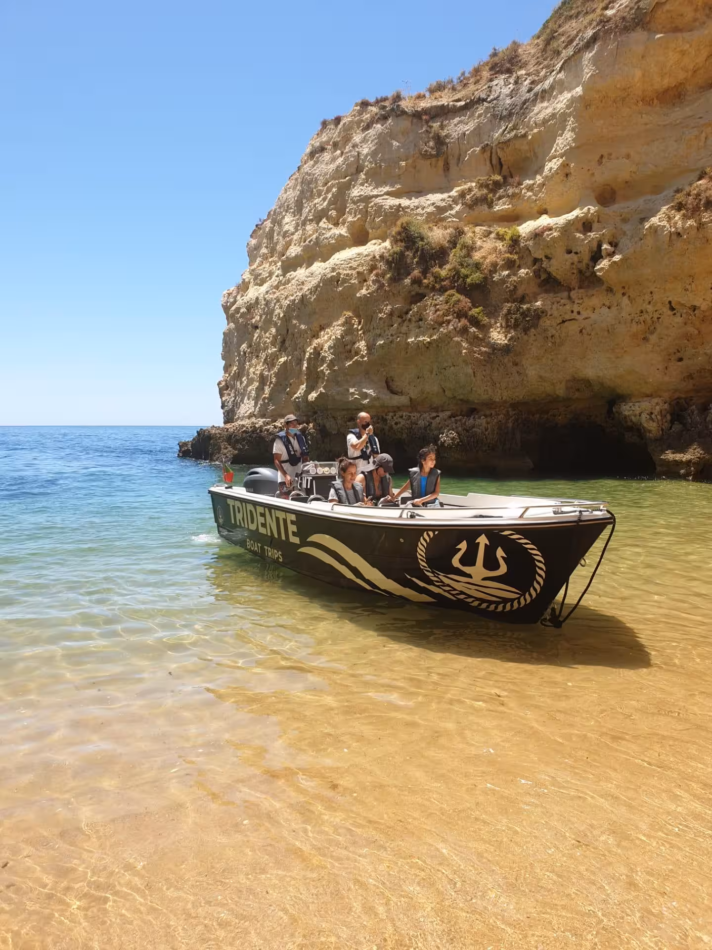 Small Tridente boat on crystal-clear water by golden cliffs during a private 1-hour Benagil Cave tour in Algarve