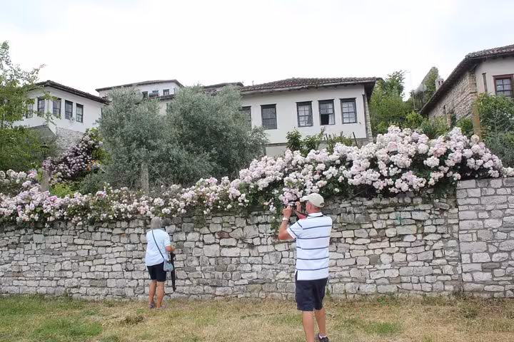 Visitors photographing traditional stone houses and floral gardens in Berat, Albania during a cultural tour.