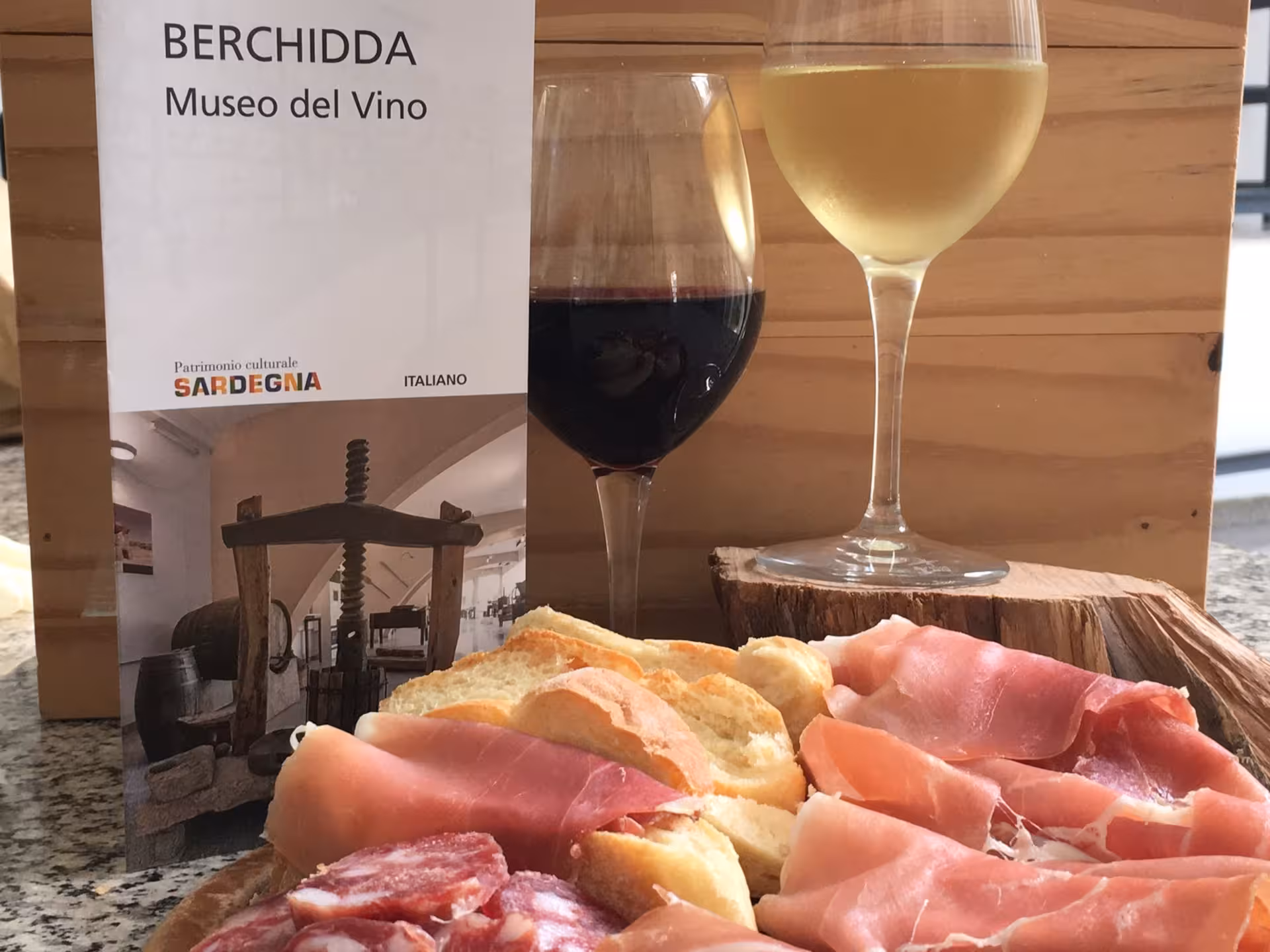 Wine tasting setup at Berchidda Wine Museum with red and white wine, cured meats, and bread showcasing Sardinian flavors.