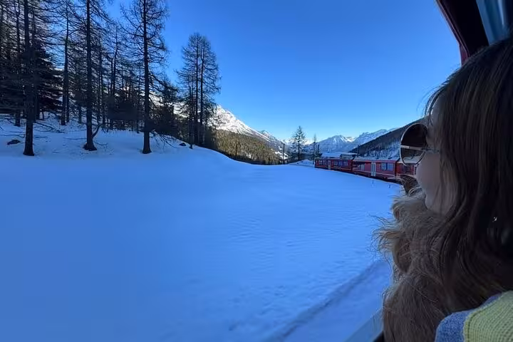 Passenger views snowy Engadin valley and alpine peaks from Bernina Express window en route to St. Moritz