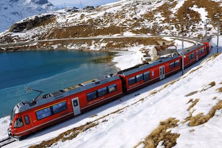 Red Bernina Express train by turquoise mountain lake on the route to St. Moritz in the Swiss Alps