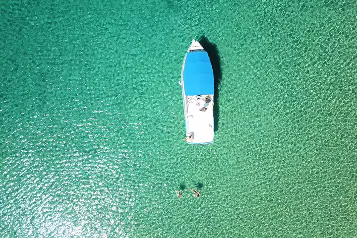 Top-down view of speedboat and swimmers in crystal-clear water on Blue Cave and 5 Islands island-hopping tour