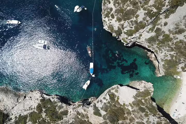Drone view of boats anchored by rocky cove and emerald lagoon on Blue Cave & 5 Islands speedboat tour