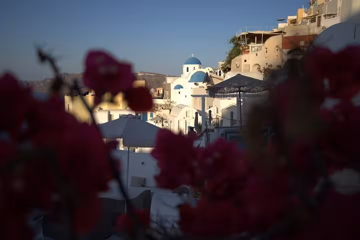 Blue-domed church in Oia framed by bougainvillea at sunset, Iconic Highlights Tour Santorini Greece