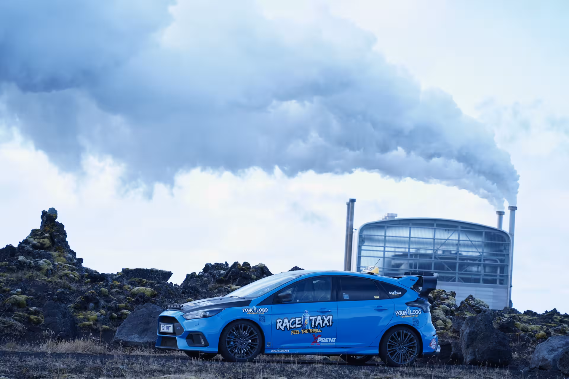 Blue rally car by geothermal plant near Krýsuvík, Iceland, on high-speed geothermal sprint tour