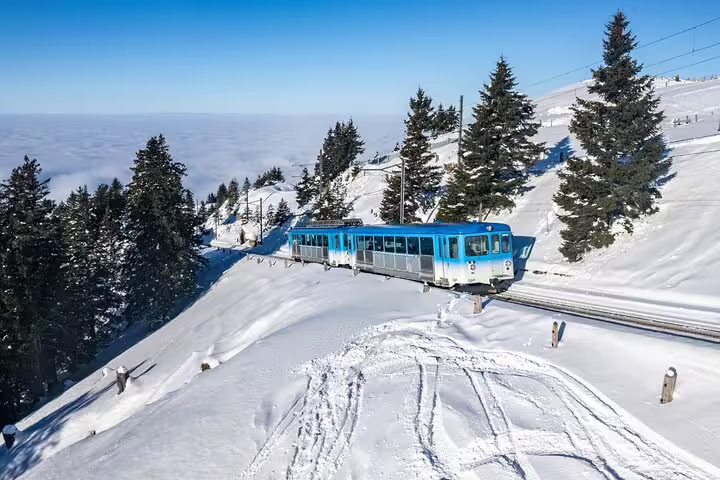 Blue train traversing snowy Mount Rigi offering panoramic winter views on a scenic Swiss day trip.