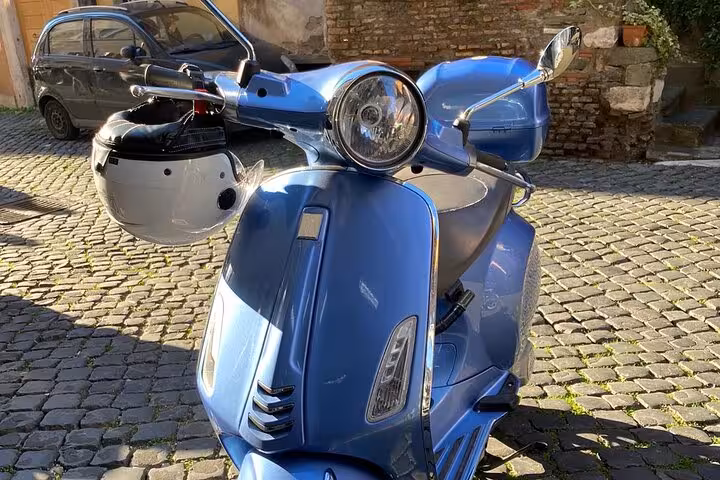 Close-up of a stylish blue Vespa scooter parked on cobblestone street, ready for an exclusive Rome by night tour.