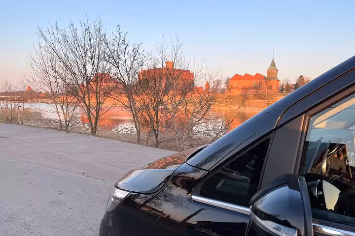 Luxury black car parked by a scenic riverside with historic architecture near Bologna airport transfer service.