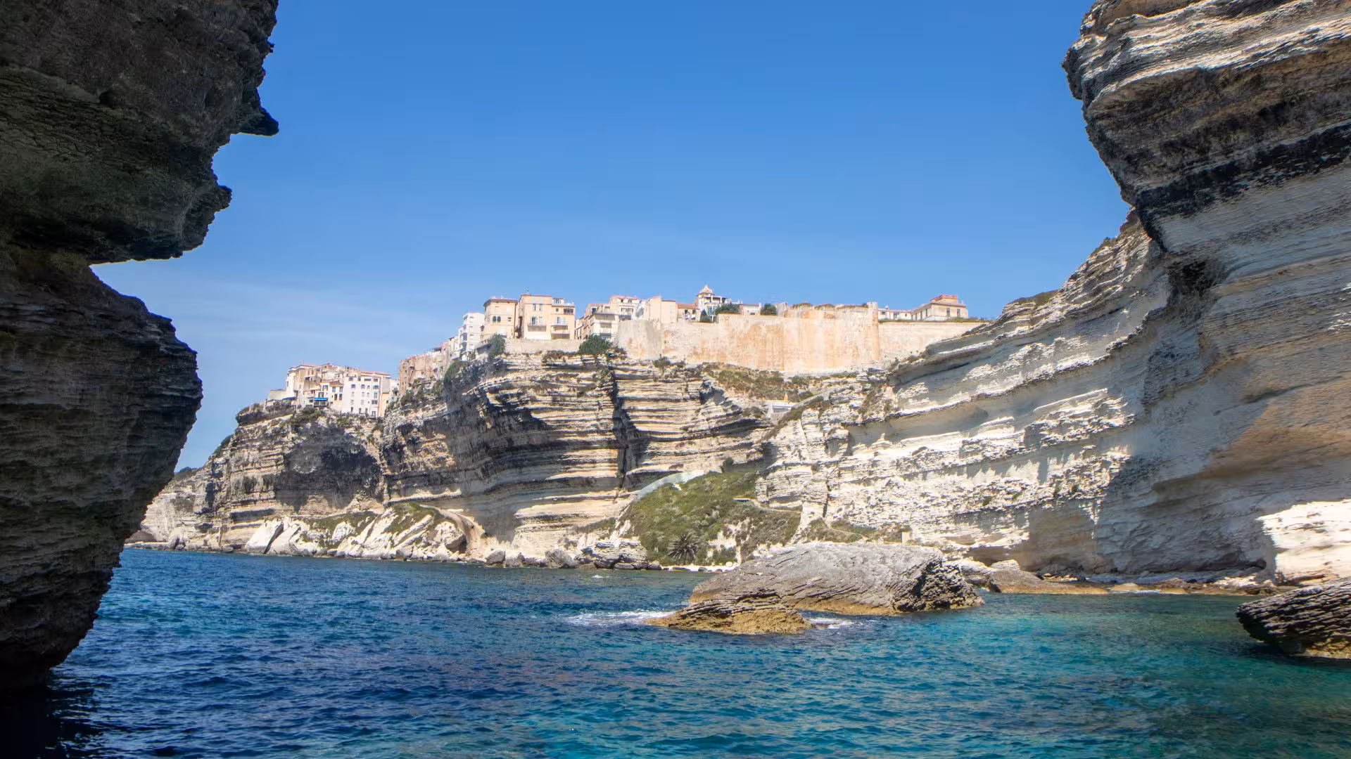 Dramatic limestone cliffs of Bonifacio framing the vibrant blue waters of southern Corsica from a dinghy tour.