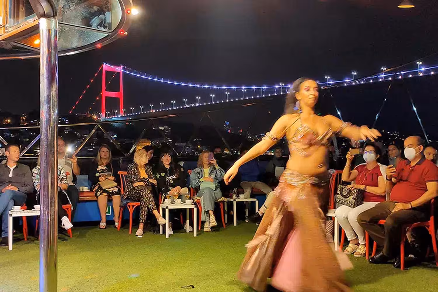Belly dancer performing on Bosphorus dinner cruise with Istanbul skyline and Bosphorus Bridge lights in background