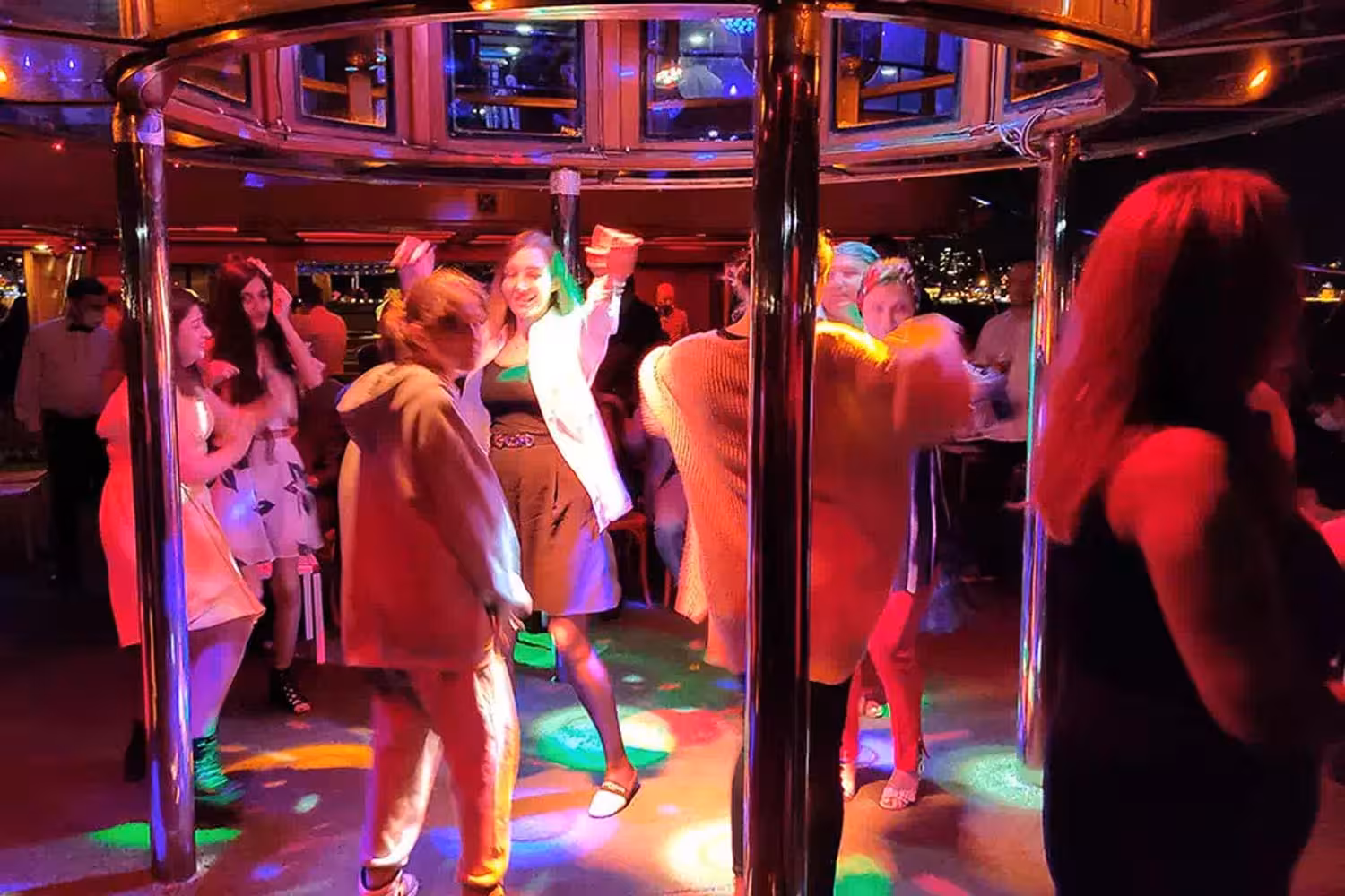 Guests dancing under colorful lights on a Bosphorus dinner cruise in Istanbul with onboard DJ party vibe