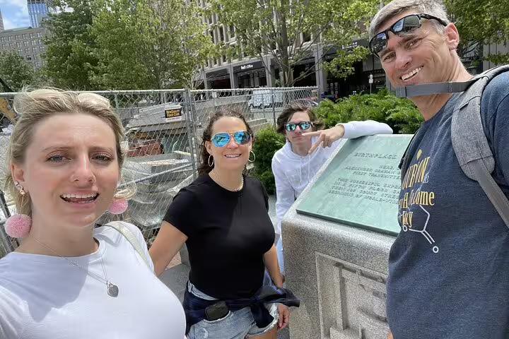 Group of four tourists smiling at historic Boston landmark plaque during self-guided walking tour