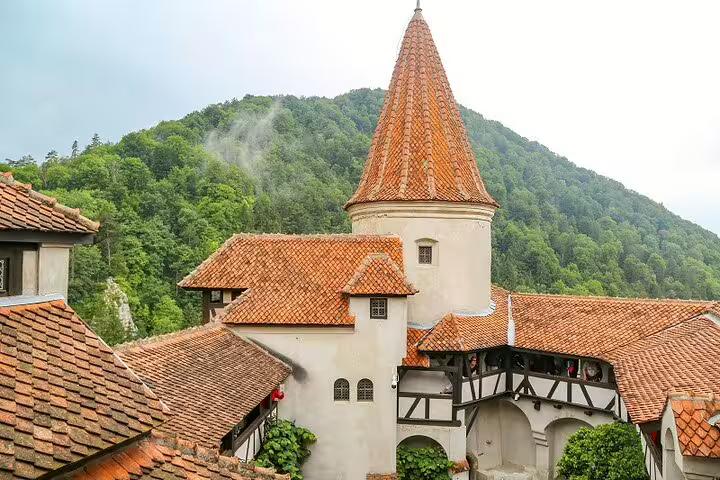 Bran Castle courtyard with orange terracotta rooftops and round tower, surrounded by forested mountains in Transylvania