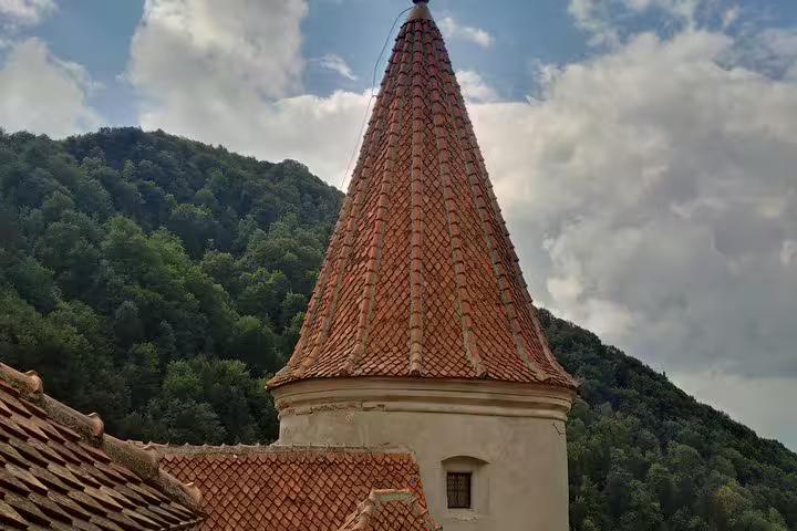 Conical red-tiled tower of Bran Castle with forested hills in background, Brasov Romania