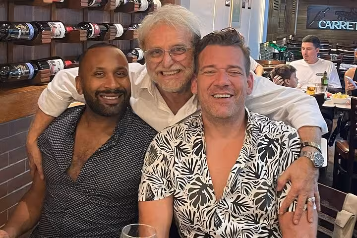 Three smiling people enjoying wine in a cozy Rio restaurant, surrounded by bottles and a lively atmosphere.
