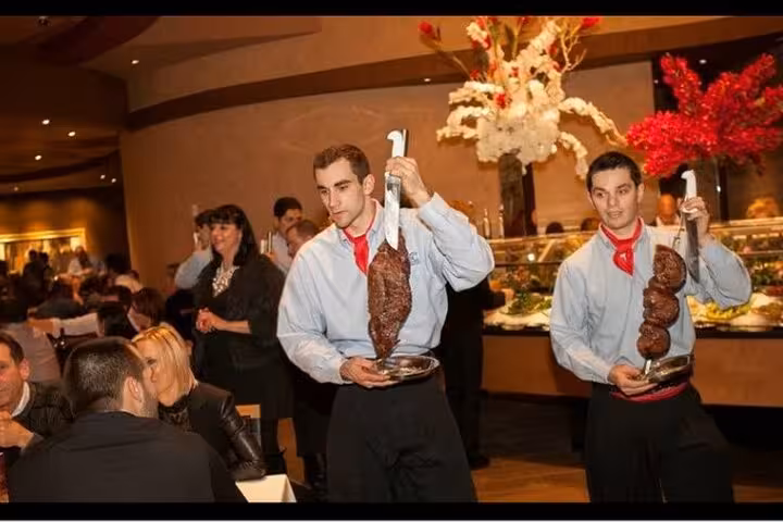 Waiters serving skewered meats in a vibrant Brazilian BBQ restaurant, capturing the lively ambiance of a Rio dinner event.