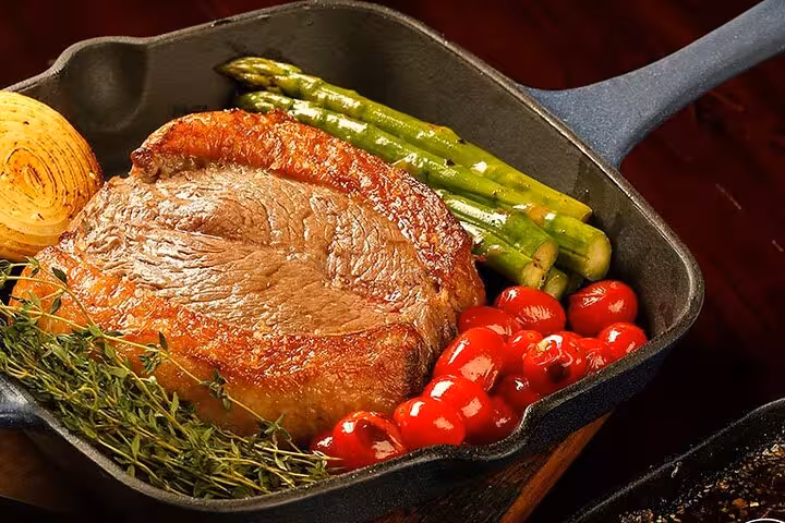 Delicious Brazilian BBQ steak with asparagus, cherry tomatoes, and herbs in a skillet from Rio dining experience.