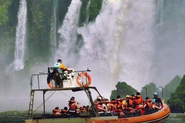 Tourists enjoy a thrilling boat ride near the majestic Brazilian Falls, surrounded by lush greenery and cascading water.