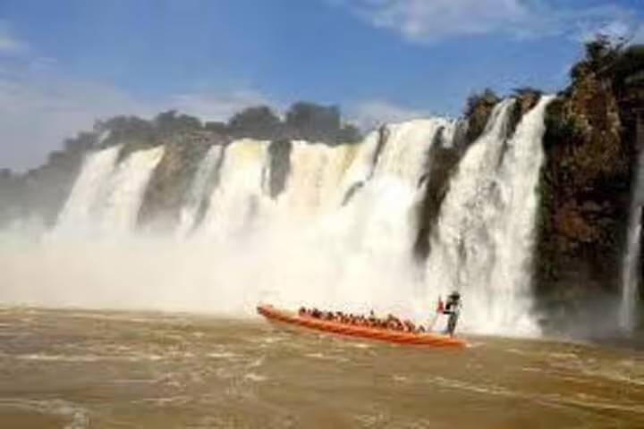 Tourists enjoy a thrilling boat ride near the majestic Brazilian waterfalls under a clear blue sky.