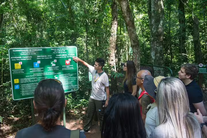 Tour group listening to a guide explaining safety instructions at a signpost in the Brazilian rainforest.