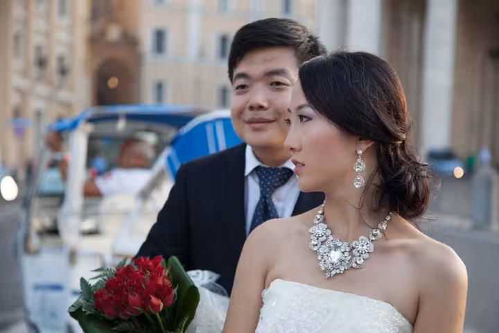 Bride and groom pose for a romantic photo during a Valentine buggy tour in Rome, holding a bouquet of red flowers.
