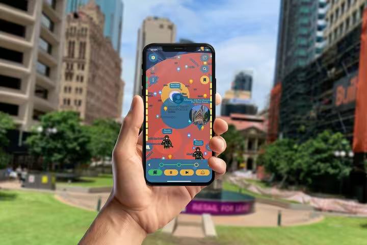 Hand holding phone with interactive Brisbane mystery walking tour app map near historic city landmarks