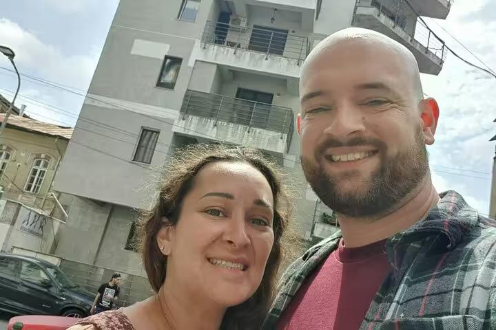 Smiling couple taking a selfie in front of a communist-era apartment block in Bucharest