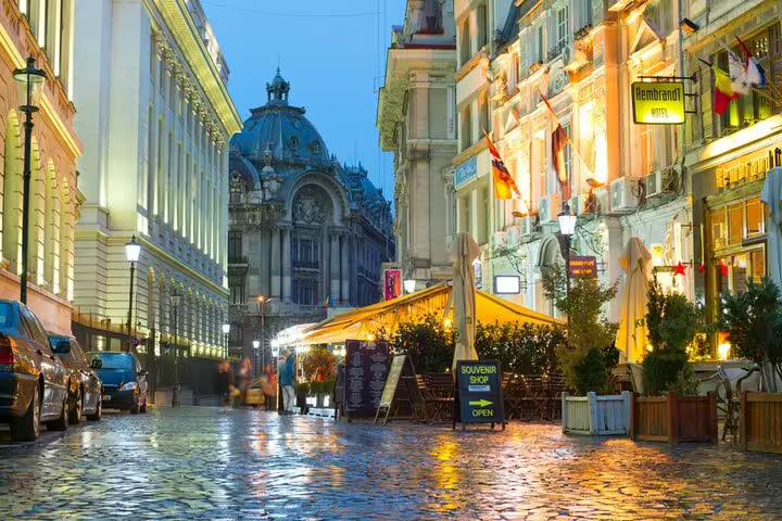 Rainy cobblestone street in Bucharest Old Town at night with glowing restaurants and historic buildings