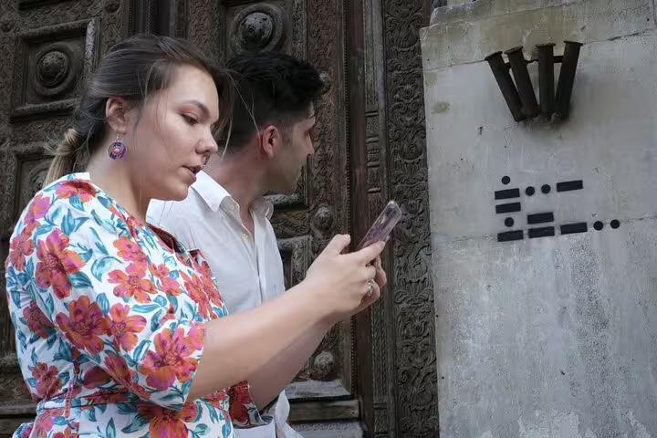 Two tourists scanning a Morse code clue on a stone wall during a self-guided walking tour in Bucharest Old Town