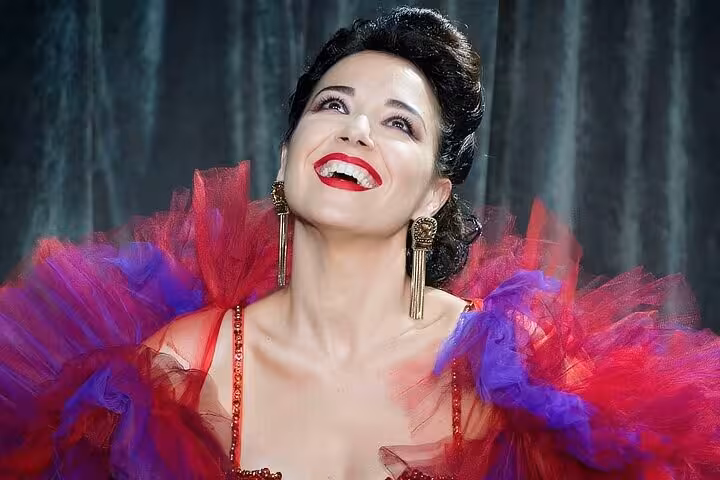 Glamorous burlesque performer in red and purple tulle smiles on stage during The Burlesque Experience of Rome with Verissima Show