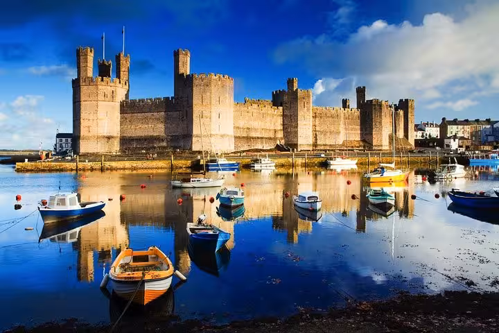 Caernarfon Castle reflected in harbor with moored boats, featured on Portmeirion Castles and Snowdonia tour