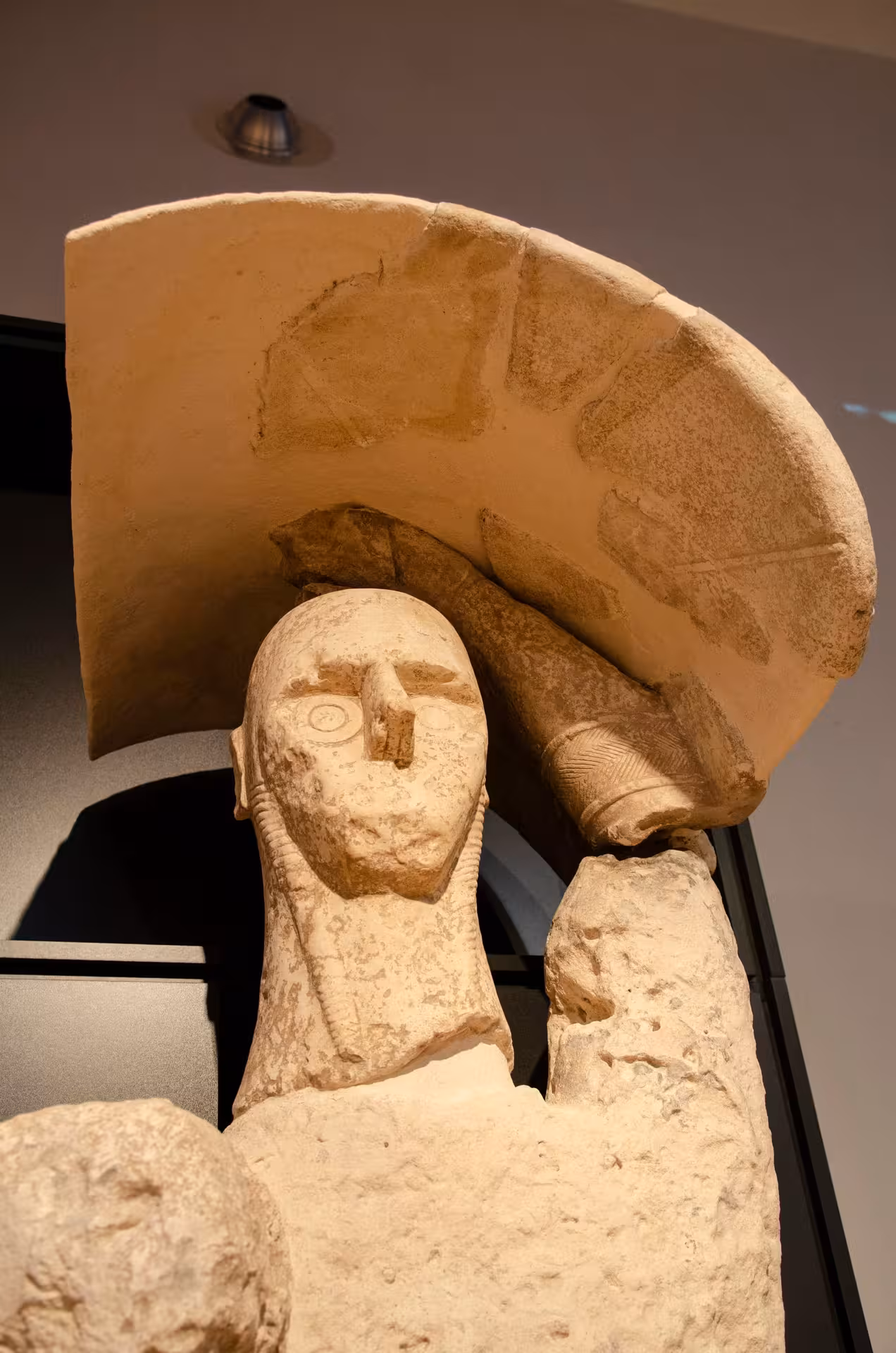 Close-up of a weathered stone statue with a distinctive flat headpiece at Cagliari's Archaeological Museum.
