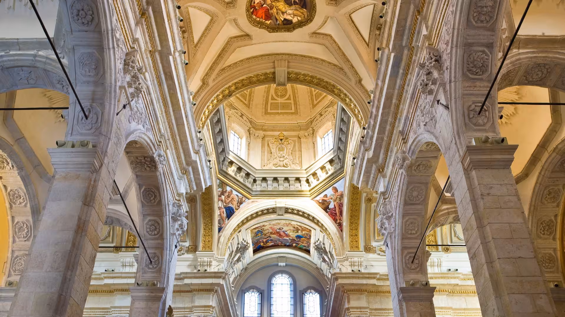 Interior view of Cagliari Cathedral featuring elaborate arches, detailed frescoes, and natural light.