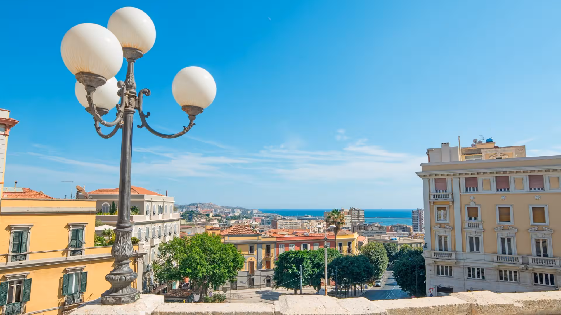 Charming street lamp overlooking Cagliari's historic center with sea views and historic architecture under clear skies.