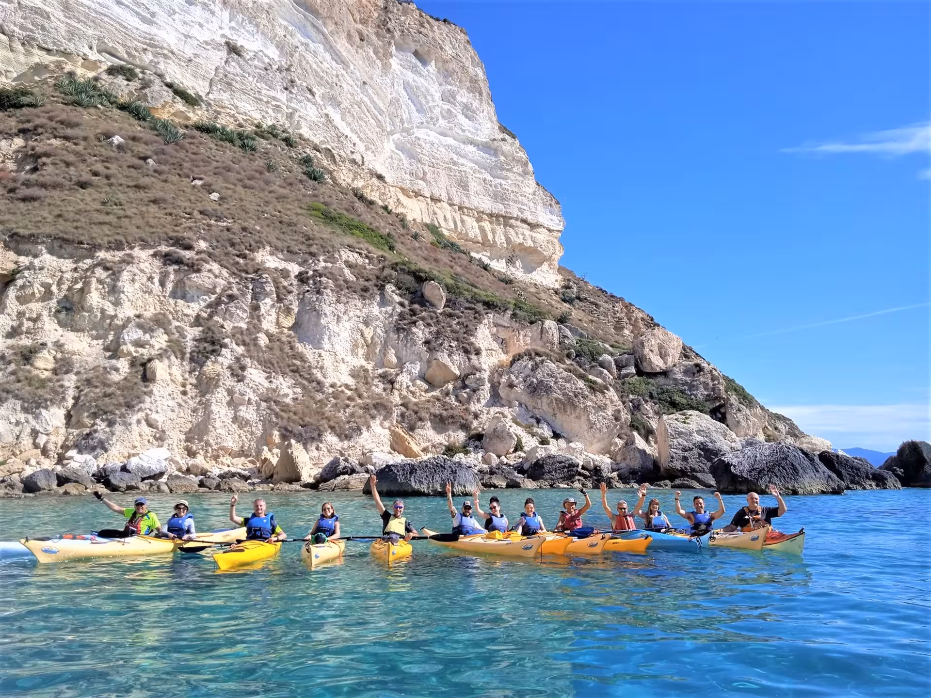 Group kayaking near the scenic cliffs of Cagliari, enjoying a sunny day on crystal-clear Mediterranean waters.