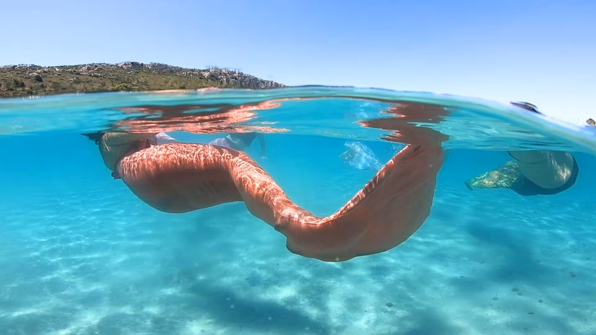 Underwater view of a swimmer in a shimmering mermaid tail in Cagliari's crystal-clear Gulf of Angels.