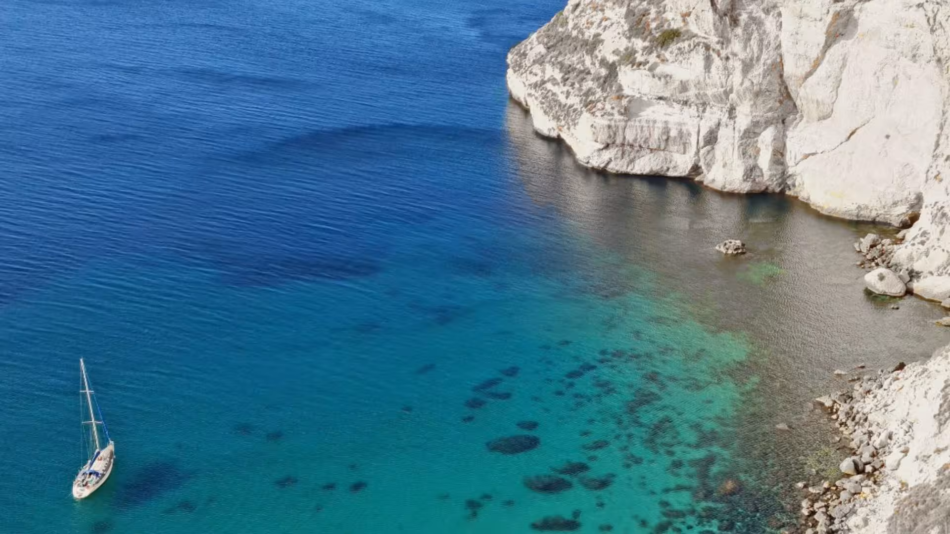 Sailboat anchored near rocky cliffs in the serene, clear waters of Mari Pintau, Cagliari, ideal for exploration.