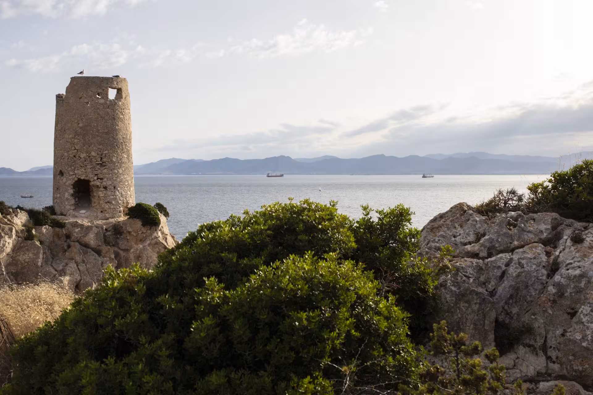 Ancient stone tower overlooking the Gulf of Cagliari, surrounded by rugged cliffs and lush vegetation on Sant'Elia hill.