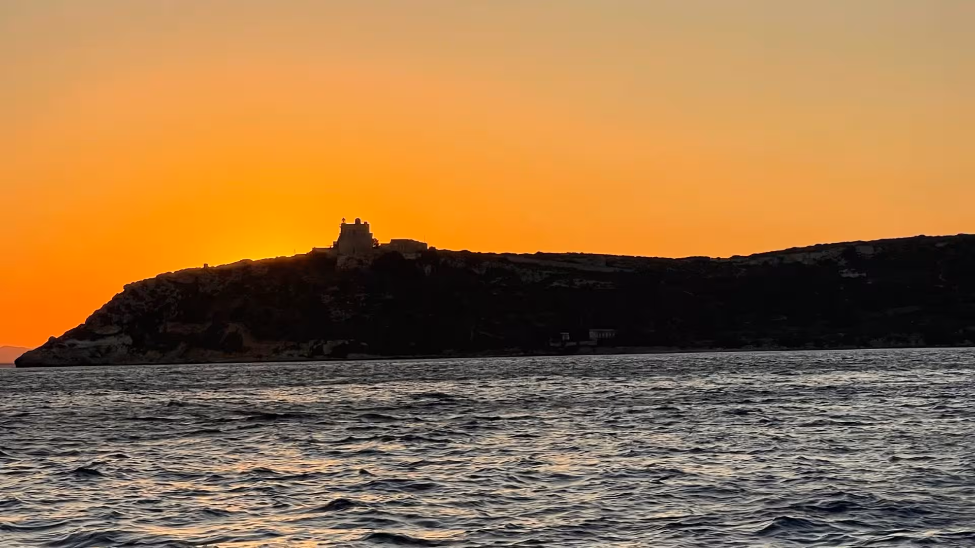 Stunning sunset silhouette of a historic building on the Cagliari coast during a scenic dinghy tour.